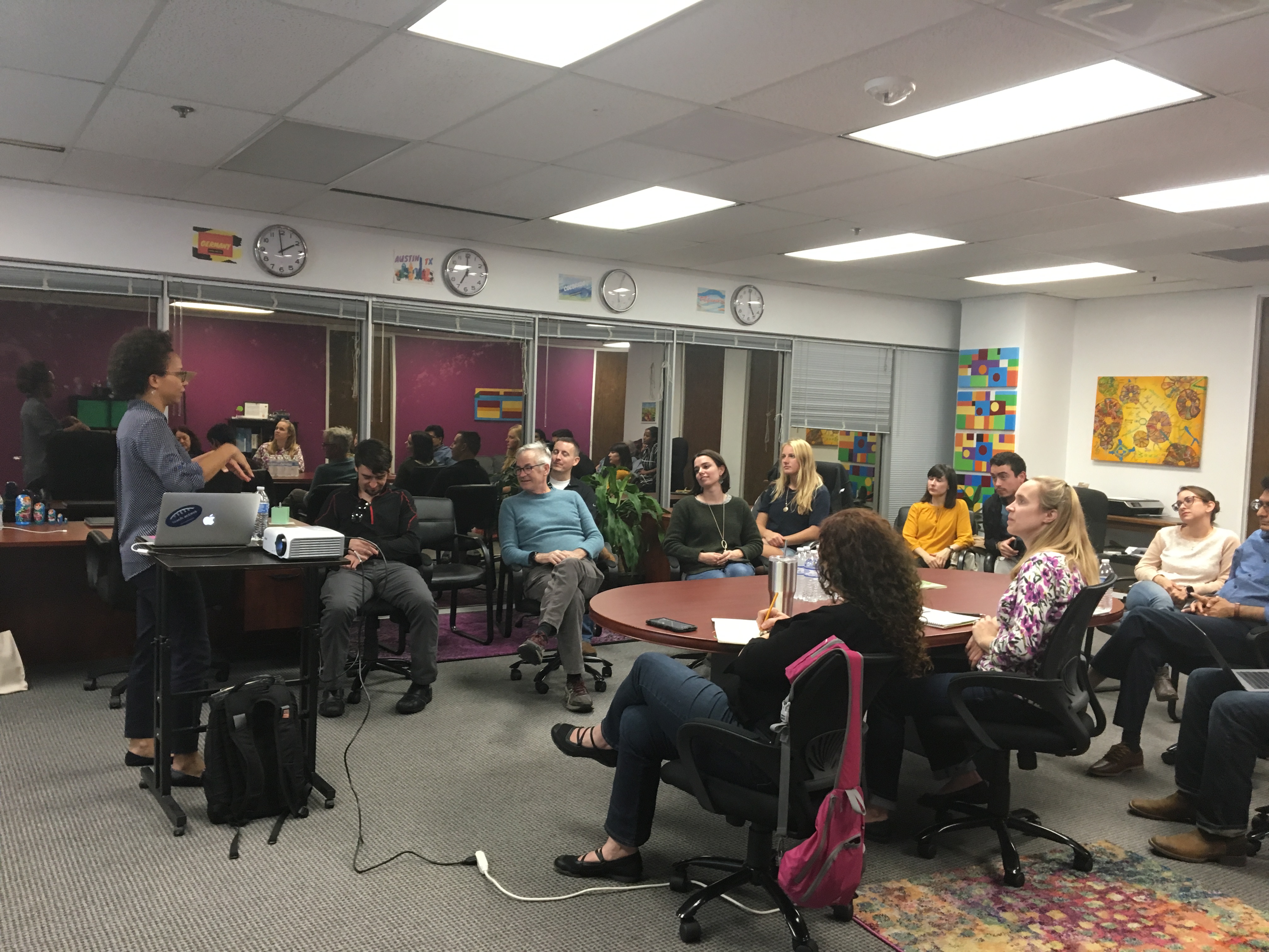 A woman giving a presentation in the Knowbility office. Attendees are seated in a circle listening to the speaker.